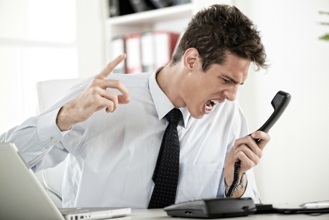 Angry young Businessman sitting in the office and screaming on the phone.